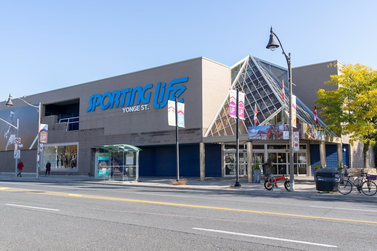 Front of a Sporting Life retail store on Yonge Street with a glass pyramid entrance and blue signage under a clear sky.