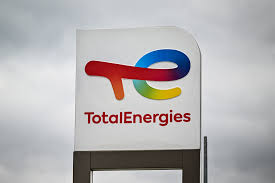 TotalEnergies signboard with the rainbow-colored swoosh logo and the brand name against a cloudy sky.