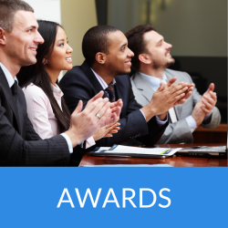 Group of five professionals applauding at an awards ceremony, seated at a table with documents in front of them.