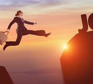 Businessperson in a suit jumps across a chasm toward a rock with large 'JOB' letters at sunset, symbolizing pursuing a new opportunity.