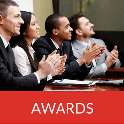 Group of diverse professionals applauding at an awards ceremony, with a red 'AWARDS' banner in front.