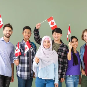 Group of diverse young adults smiling and waving small Canadian flags together against a green background.