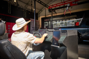 Person wearing a straw hat driving a race-car simulator cockpit, hands on the steering wheel, side seats visible