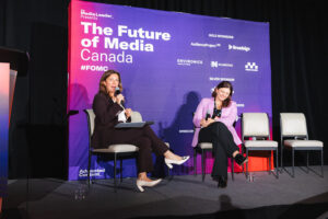Two women panelists sit on a stage with microphones, a purple backdrop reads'The Future of Media Canada' with sponsor logos behind them.