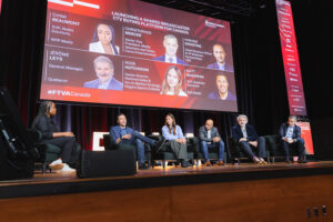 Panel of six people seated on stage during a conference; a large screen behind shows speaker bios and the hashtag #FTVACanada.