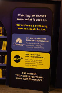 Tall sign with messaging about streaming ads, featuring a Paramount+ blue panel and a Pluto TV yellow panel with logos and service descriptions.