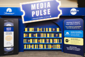 Blue display with a large'Media Pulse' sign and shelves of yellow-tashed VHS-like cases, Paramount+ and Pluto TV logos visible.