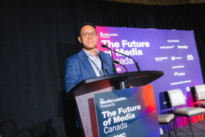 Speaker at a podium during a conference, banner reads'The Future of Media Canada' on stage behind him.