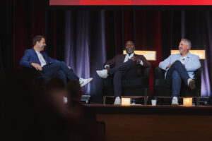 Three men seated in armchairs on a stage, engaged in a panel discussion.