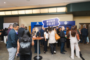 Crowd of professionally dressed people networking at a media event with a'Media Pulse' sign in the background.