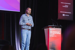Speaker on stage delivering a talk at a conference, standing by a podium with'The Future of TV Advertising Canada' sign visible.
