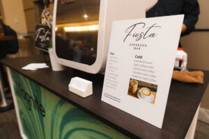 Counter at a coffee bar with a Fiesta Espresso Bar menu card and brochure on the dark counter; a white device sits nearby.