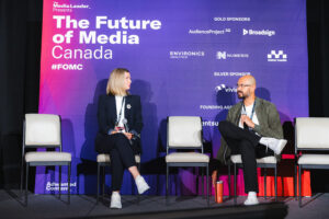 Two panelists sit on stage with a purple backdrop that reads'The Future of Media Canada' during a discussion.