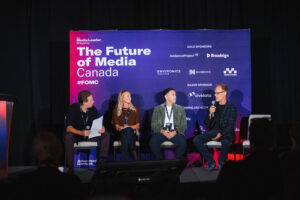 Panel discussion on stage with four speakers in front of a purple backdrop that reads'The Future of Media Canada'.