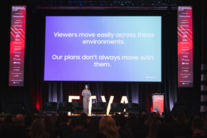 Speaker on stage presenting a slide that reads,'Viewers move easily across those environments. Our plans don’t always move with them.'