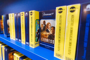 Row of VHS tapes on a blue shelf, with a prominent'Lioness' cover from Paramount+ in the center of the lineup.