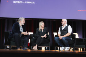 Three panelists seated in armchairs on a stage during a discussion, with a purple screen behind showing'QUEBEC → CANADA'.