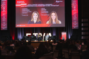Panel discussion on stage at a conference, two women speakers seated with a large screen behind them.